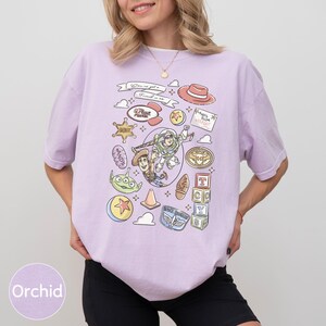 A woman wearing a purple t-shirt with various cartoon-style icons and characters printed on it.