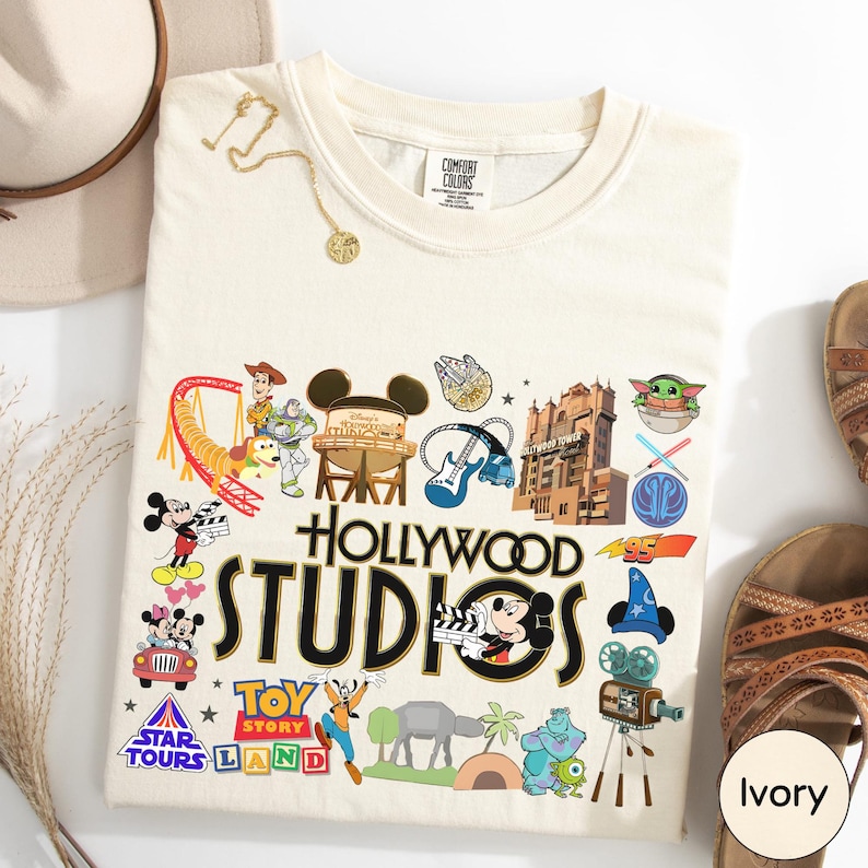 a white t-shirt with various Disney and Pixar-themed graphics and logos, including Mickey Mouse, Minnie Mouse, Toy Story, Star Tours, and the Hollywood Studios logo.
