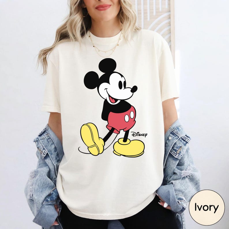 A woman wearing a white t-shirt with a Mickey Mouse graphic and yellow shoes, paired with a denim jacket.