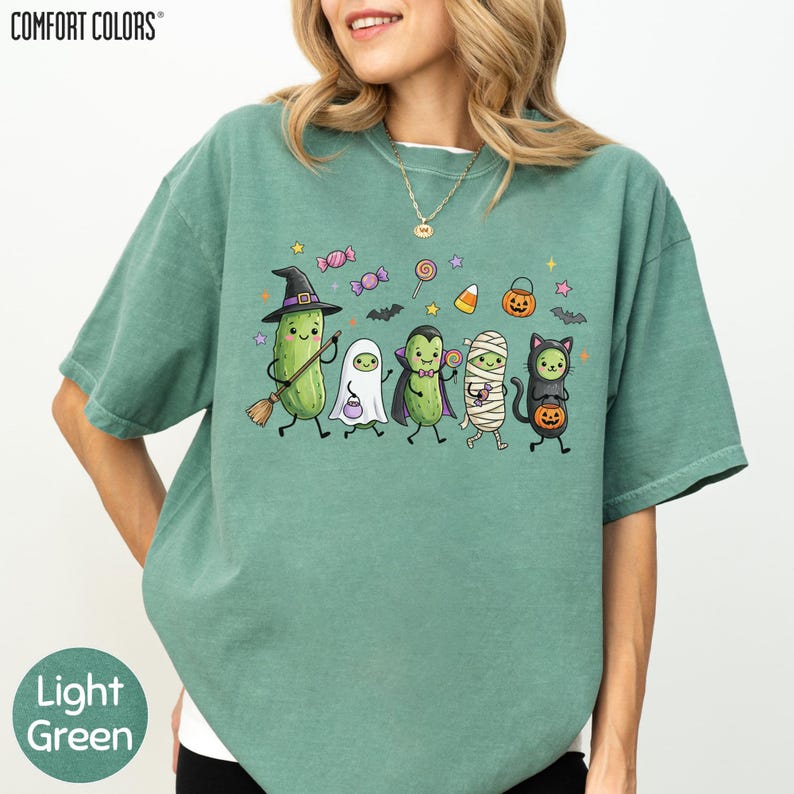 A woman wearing a green t-shirt with a graphic design of various cartoon characters, including a witch, ghost, skeleton, mummy, and jack-o-lantern, along with Halloween-themed elements.