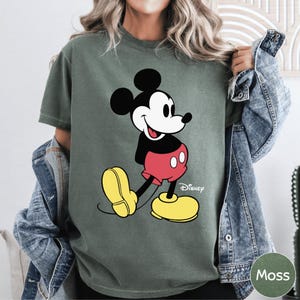 A woman wearing a green t-shirt with a cartoon image of Mickey Mouse and yellow shoes.