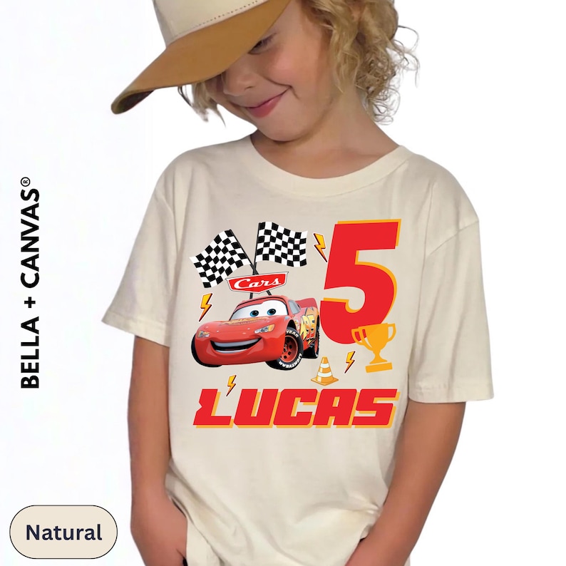 A young child wearing a white t-shirt with a graphic of a red car and the number 5, along with the text "Lucas" and a checkered flag.