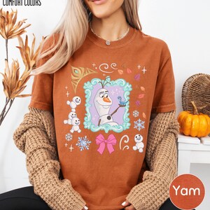 A woman wearing a brown sweater and a t-shirt with a cartoon character from the Disney movie Frozen.