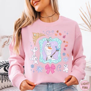A woman wearing a pink sweatshirt with a graphic of Olaf from the Disney movie Frozen.