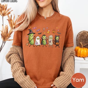 A woman wearing a t-shirt with a Halloween-themed graphic of various cartoon characters, including a witch, pumpkin, ghost, and cat, along with other Halloween-related elements.
