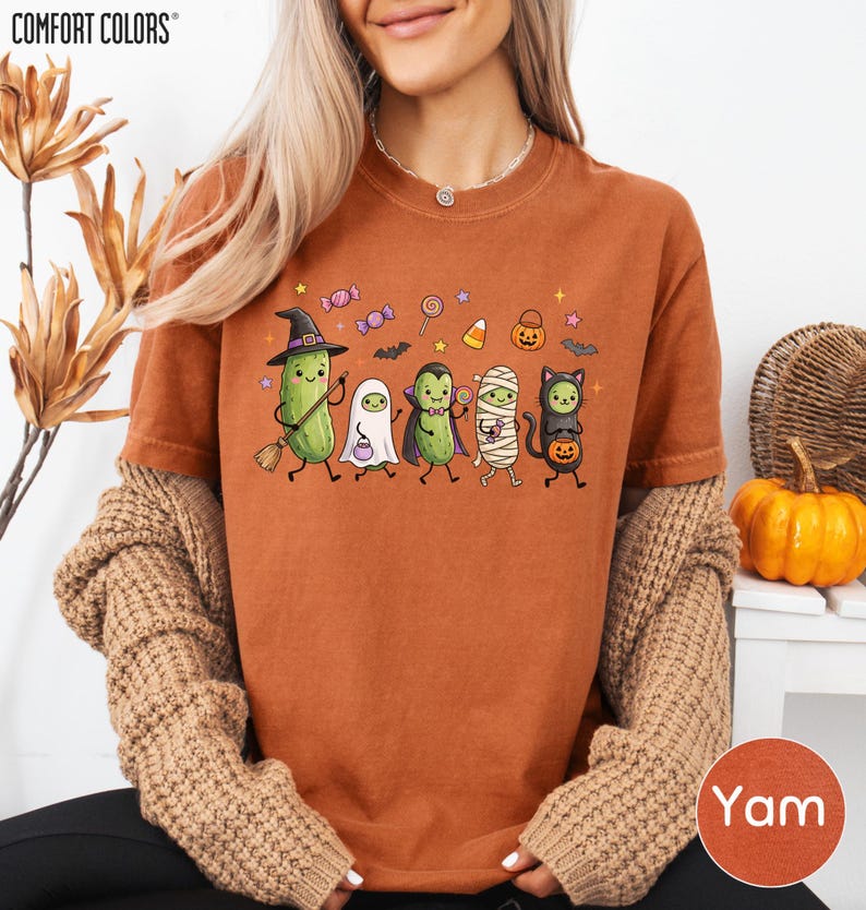 A woman wearing a t-shirt with a Halloween-themed graphic of various cartoon characters, including a witch, pumpkin, ghost, and cat, along with other Halloween-related elements.
