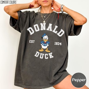 A person wearing a black t-shirt with a graphic of a cartoon duck and the text "DONALD EST. 1934 DUCK" printed on it.