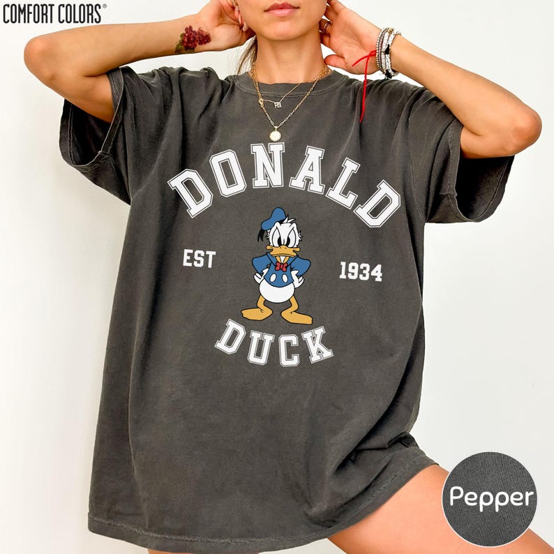 A person wearing a black t-shirt with a graphic of a cartoon duck and the text "DONALD EST. 1934 DUCK" printed on it.