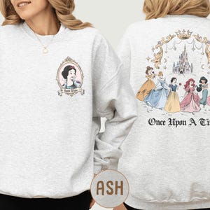 A woman wearing a grey sweatshirt with a design featuring the characters from the Disney film "Once Upon a Time".