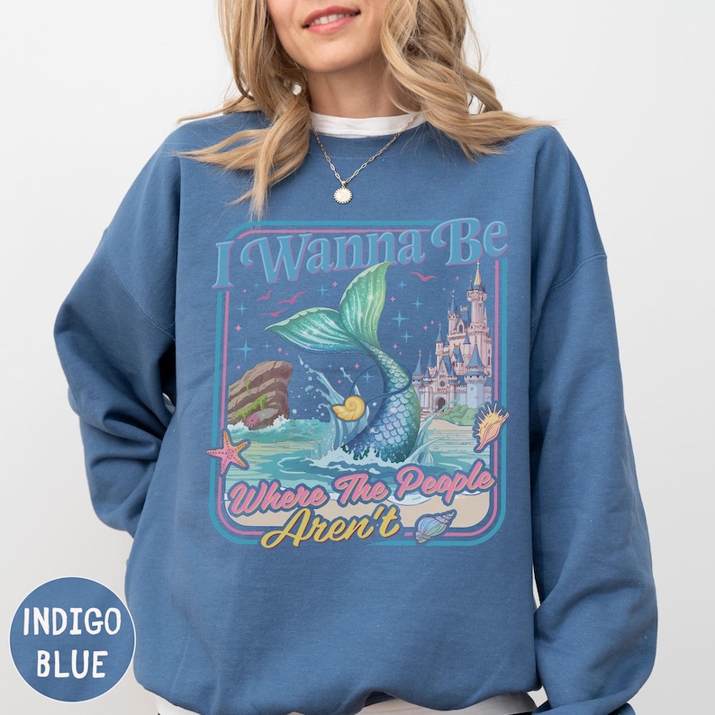 A woman wearing a blue sweatshirt with a mermaid graphic and text on it.