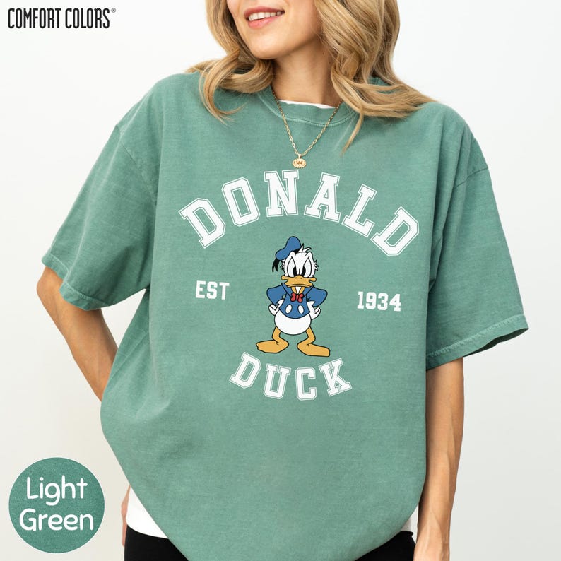 A woman wearing a green t-shirt with a graphic of a cartoon duck and text that says "DONALD DUCK EST 1934".