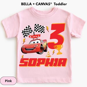 A pink t-shirt with a design featuring a red car and the text "Sophia" along with a number "3" and a checkered flag.