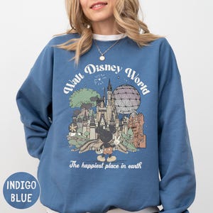 A woman wearing a blue sweatshirt with a graphic design depicting various landmarks and attractions from the Walt Disney World theme park.
