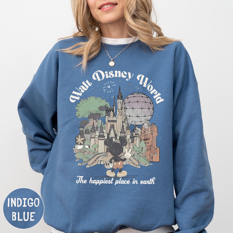 A woman wearing a blue sweatshirt with a graphic design depicting various landmarks and attractions from the Walt Disney World theme park.