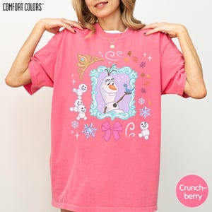 A woman wearing a pink t-shirt with a cartoon character from the Disney movie Frozen.