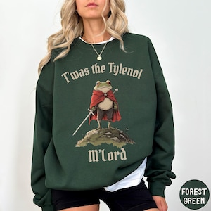 May include: Forest green sweatshirt with the text "T'was the Tylenol M'Lord" and a cartoon frog wearing a red cape and holding a sword. The frog is standing on a small hill. The sweatshirt has a round neck.