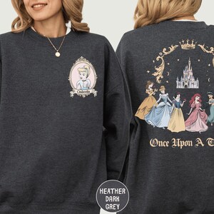 A woman wearing a gray sweatshirt with a design featuring the Disney princess characters Cinderella and the text "Once Upon a Time" on the back.