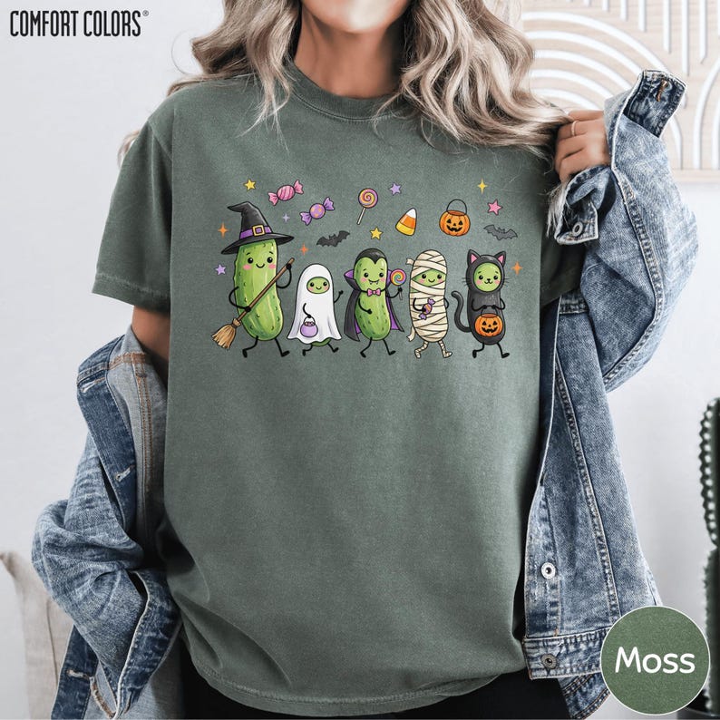A person wearing a green t-shirt with a Halloween-themed graphic of various cartoon characters, including a witch, ghost, pumpkin, and other spooky and festive figures.