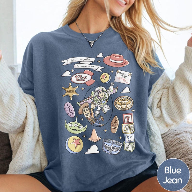 A woman wearing a blue t-shirt with a graphic design featuring various cartoon characters and icons from the Toy Story franchise.