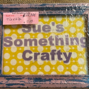 Könnte beinhalten: Ein gerahmtes Schild mit gelbem und weißem Polka-Dot-Hintergrund. Das Schild lautet "Sue's Something Crafty". Der Rahmen ist in hellblau und rosa gestrichen.
