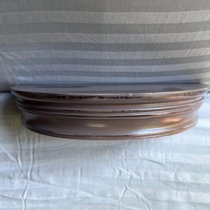 May include: A half-circle, brown wooden shelf with a decorative, layered edge. The shelf is mounted on a wall and is designed to hold small items. The wood has a slightly distressed finish.