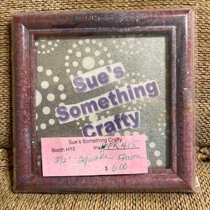 Könnte beinhalten: Ein roter Holzbildrahmen mit weißem Punktmuster als Hintergrund. Der Rahmen ist 8,9 cm quadratisch und kostet 6,00 €. Der Text auf dem Rahmen lautet "Sue's Something Crafty, Booth H10, Inv# FR 415, 3 1/2 Square Frame, 6,00 €".