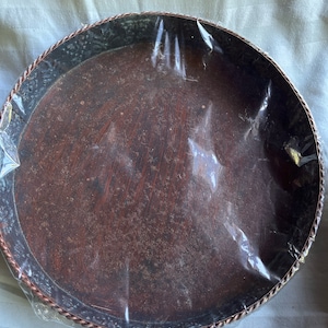 May include: A round, brown tray with a decorative metal rim. The tray is made of wood and has a rustic look.