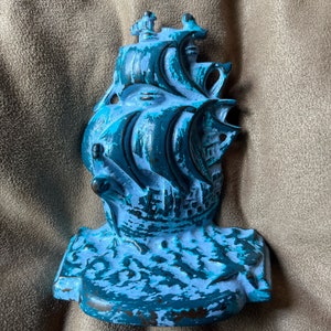 Peut inclure: Un arrêt de porte en métal peint en bleu et blanc. Le navire a un design détaillé avec des voiles et une figure de proue. L'arrêt de porte a la forme d'un navire avec une base.