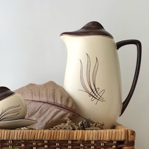 Może przedstawiać: Zestaw vintage ceramicznych naczyń kuchennych w brązowo-kremowej kolorystyce z ozdobnym wzorem liścia. Zestaw zawiera dzbanek do śmietanki, cukiernicę, dzbanek, filiżankę i spodek.