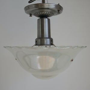 以下が含まれることがあります： 銀色の金属製のベースと、波打った縁のある白いガラスのシェードが付いた、ビンテージの天井照明器具です。