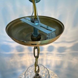 May include: A close-up view of a brass-colored ceiling light fixture. The fixture has a round, shallow shade, a chain, and a clear, patterned glass shade. A yellow wire and a metal bracket are also visible.