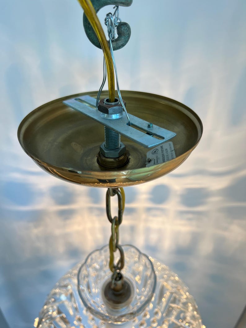 May include: A close-up view of a brass-colored ceiling light fixture. The fixture has a round, shallow shade, a chain, and a clear, patterned glass shade. A yellow wire and a metal bracket are also visible.