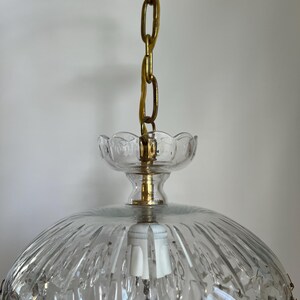 May include: A vintage clear glass chandelier with a gold-colored chain and canopy. The chandelier features a domed shade with vertical ridges and hanging crystal accents. The light fixture has a classic, elegant design.
