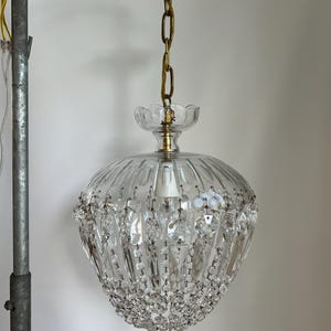 May include: A vintage crystal chandelier with a brass canopy and chain. The clear glass shade has vertical ridges and is adorned with hanging crystal accents. The fixture is suspended from the ceiling, showcasing a classic lighting design.