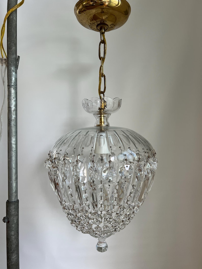 May include: A vintage crystal chandelier with a brass canopy and chain. The clear glass shade has vertical ridges and is adorned with hanging crystal accents. The fixture is suspended from the ceiling, showcasing a classic lighting design.