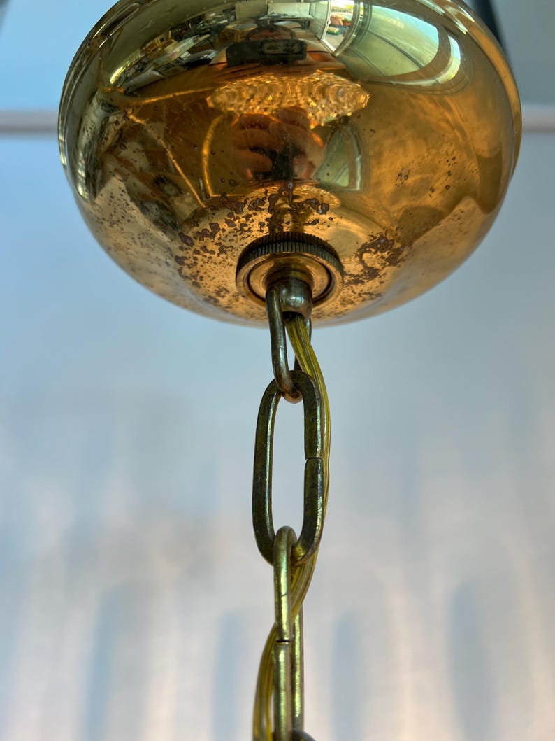 May include: Close-up of a vintage brass ceiling light fixture. The fixture features a rounded, tarnished brass canopy with a chain and a small metal connector. The chain is a gold color.