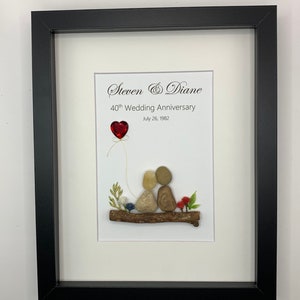 May include: A framed artwork featuring a couple made of stones sitting on a branch with a red heart balloon. The text reads "Steven & Diane 40th Wedding Anniversary July 26, 1982".