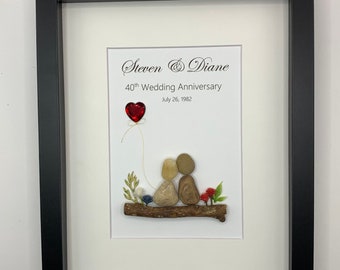 May include: A framed artwork featuring a couple made of stones sitting on a branch with a red heart balloon. The text reads "Steven & Diane 40th Wedding Anniversary July 26, 1982".