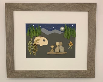 May include: A framed artwork depicting a couple and their dog sitting by a camper under a starry night sky. The artwork is made of small stones and other natural materials.