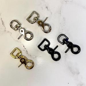 May include: Four metal swivel clasps in gold, silver, and black. The clasps are used for attaching straps or leashes to bags, purses, or other items.
