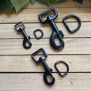 May include: Four black metal clasps and D-rings of varying sizes. The clasps have a spring-loaded gate and a swivel hook. The D-rings are round with a smooth finish.