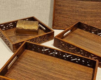 Può includere: Un set di tre vassoi rettangolari in legno marrone scuro con intricati motivi intagliati sui lati e manici integrati, accompagnato da una piccola scatola rettangolare in metallo dorato testurizzato posta all'interno di uno dei vassoi.