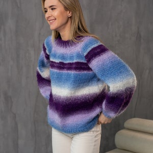May include: A woman wearing a purple, blue, and white striped fuzzy sweater with long sleeves. She is smiling and looking to the right.