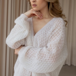 May include: A white, lightweight, open knit cardigan with a v-neck and button closure.