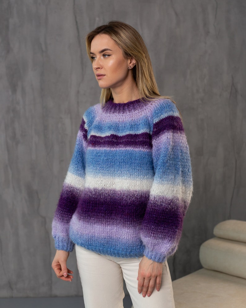 May include: A striped sweater with a gradient of purple, blue, and white. The sweater has a relaxed fit and long sleeves.