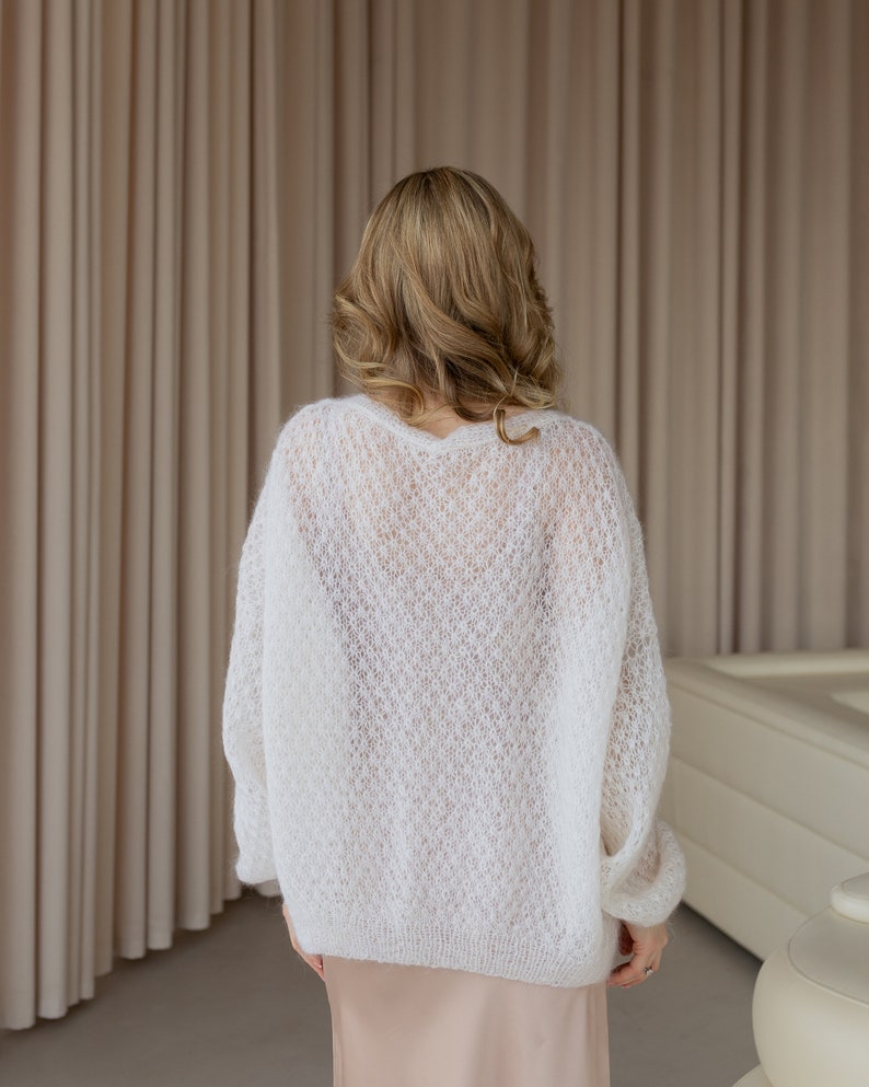 May include: A white, open-knit sweater with a loose fit. The sweater is made of a soft, delicate yarn and has a relaxed, casual style.
