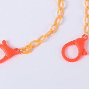 May include: A yellow and orange plastic chain with two orange plastic clasps. The chain is made of oval links.