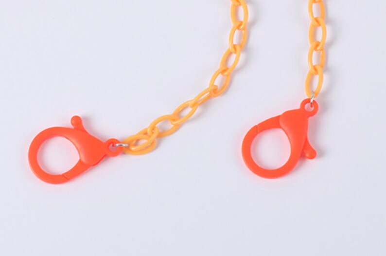 May include: A yellow and orange plastic chain with two orange plastic clasps. The chain is made of oval links.