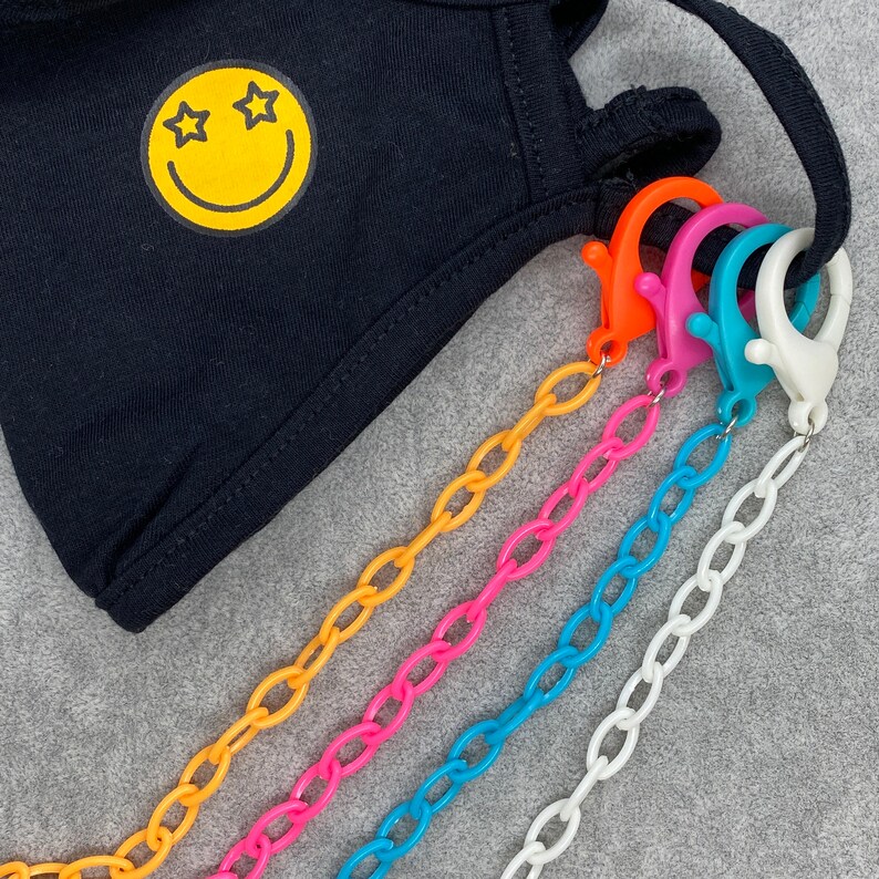 May include: Five colorful plastic chains with lobster clasps attached to a black face mask with a yellow smiley face with stars for eyes.