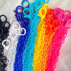 May include: A rainbow assortment of colorful plastic chains with lobster clasps. The chains are arranged in a rainbow pattern, starting with black, white, blue, light blue, yellow, orange, and pink.
